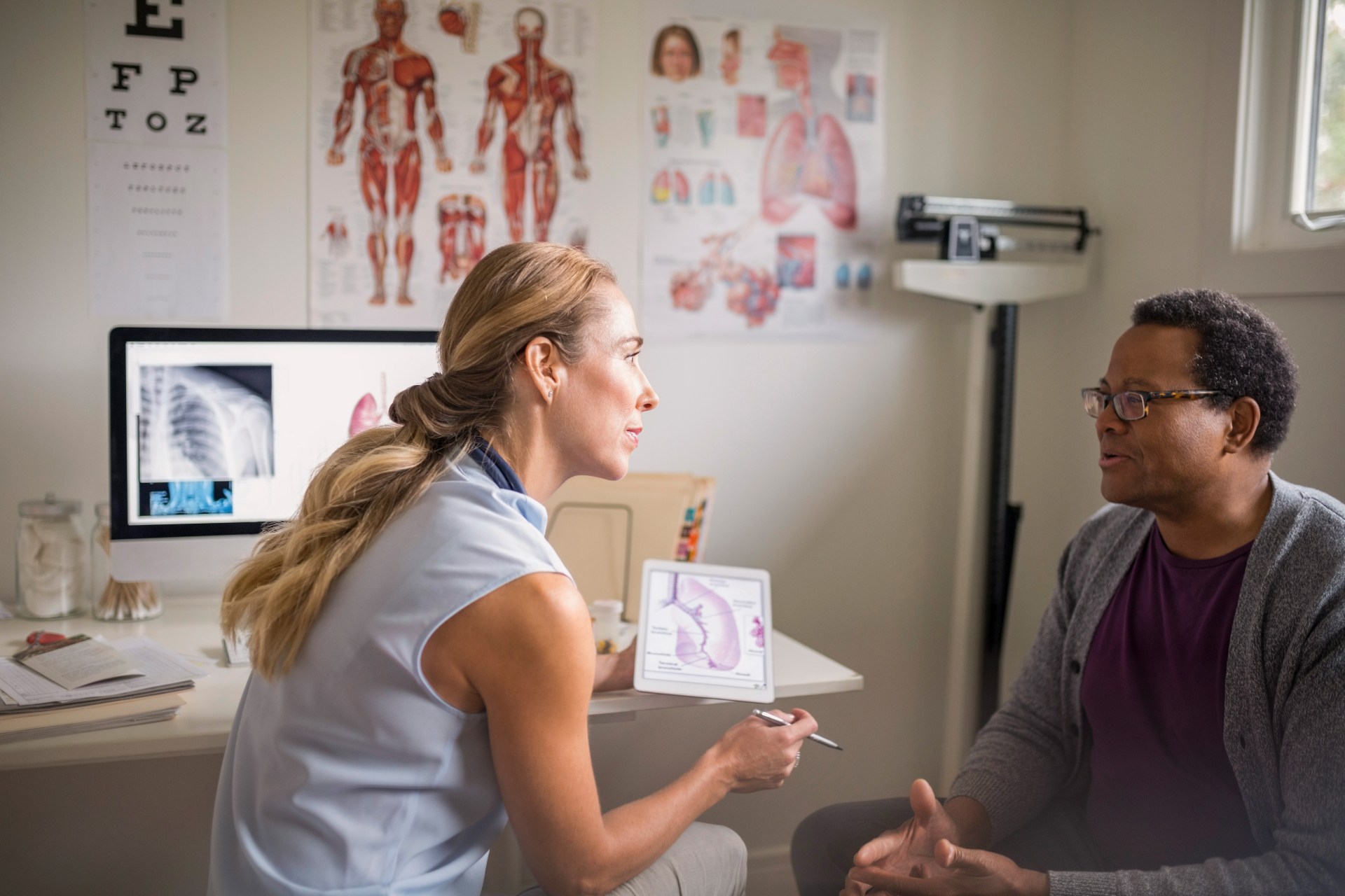 Female doctor with digital tablet talking with senior male patient in examination room