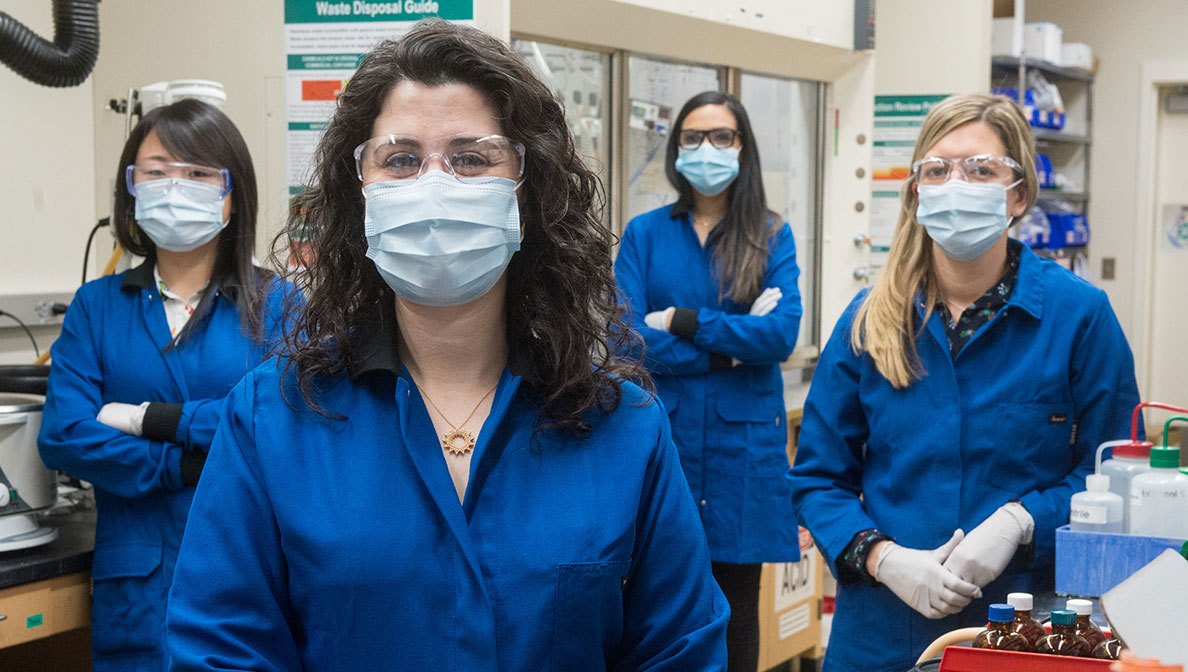 Four women scientists wear marks and glasses in a lab